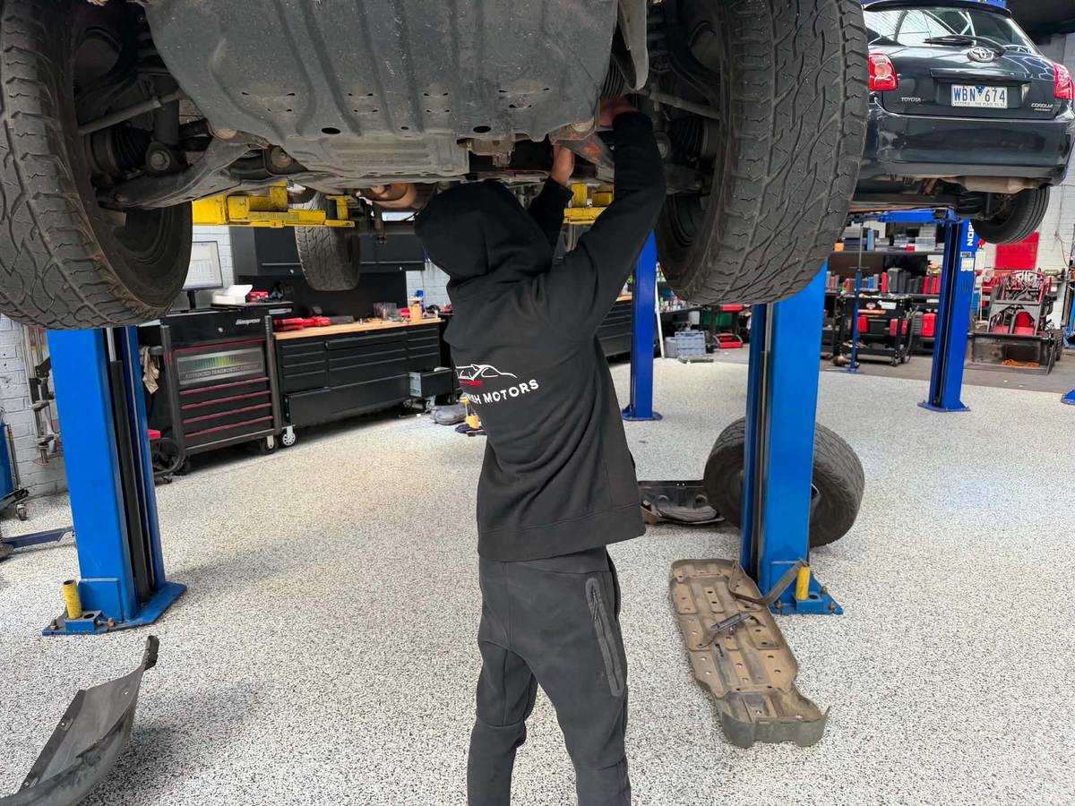 A Darwish Motors mechanic in a branded hoodie working underneath a car raised on the hoist