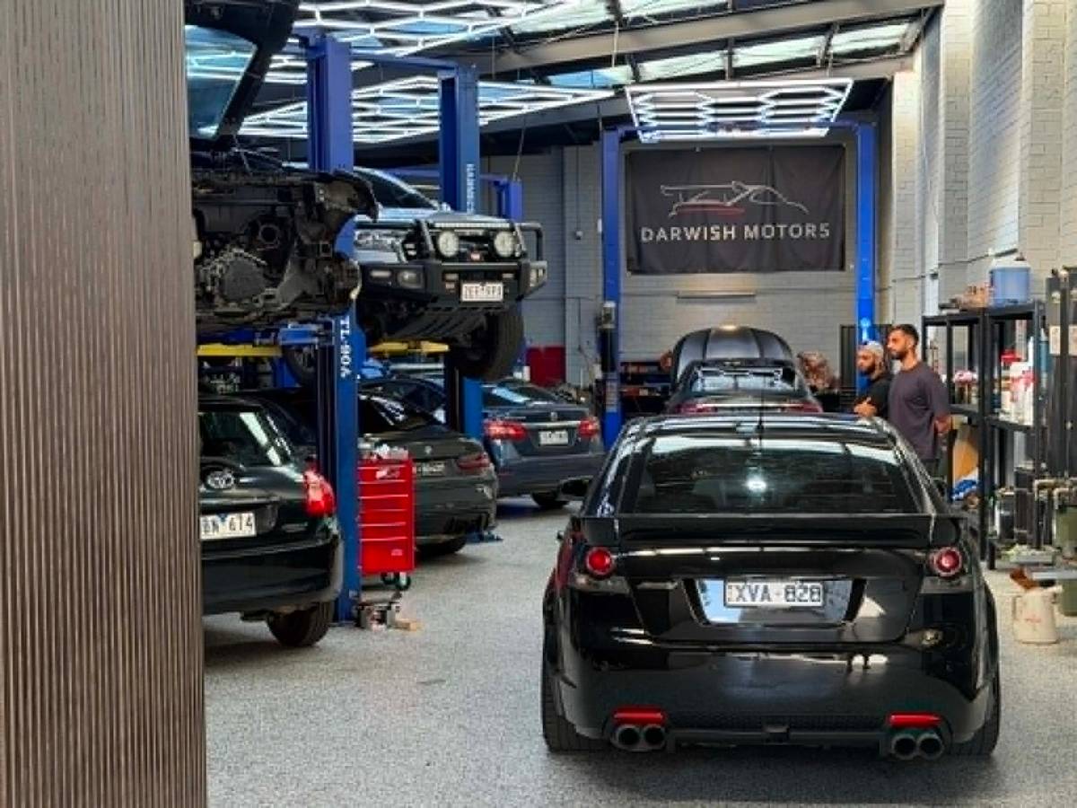 A wide view inside the Darwish Motors workshop in Brunswick: several cars on hoists with the team at work and the Darwish Motors sign overhead